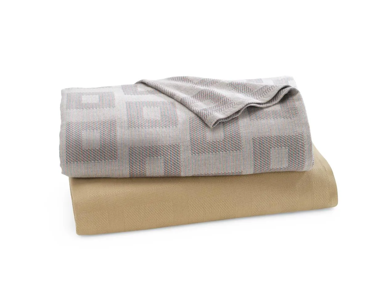 Folded jacquard cotton blanket in a grey block weave, paired with a plain gold blanket